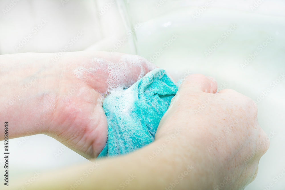 Fototapeta premium Closeup of female hands with freckles with a wet cloth. The girl washes clothes by hand.