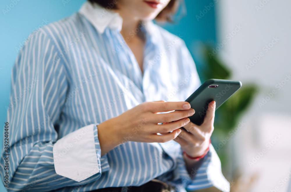 Young woman using mobile phone while working at home with laptop. The girl chatting with friends in social network, shopping online, writing email using phone. Technology, freelance and work concept. Young woman using mobile phone while working at home with laptop. The girl chatting with friends in social network, shopping online, writing email using phone. Technology, freelance and work concept.