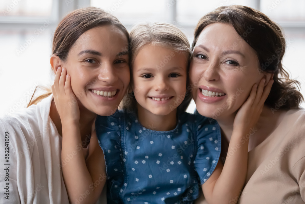 Portrait of little preschooler girl hug smiling young mother and senior grandmother, happy three generations of women embrace cuddle, enjoy family reunion, weekend at home together, bonding concept Portrait of little preschooler girl hug smiling young mother and senior grandmother, happy three generations of women embrace cuddle, enjoy family reunion, weekend at home together, bonding concept
