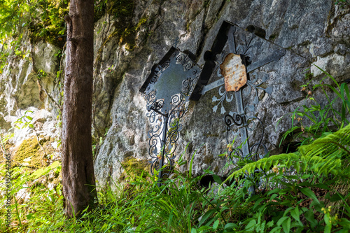 View of two ancient overgrown tombs with forged crosses at a rock face at the cemetery of Hallstatt, Salzkammergut region, OÖ, Austria