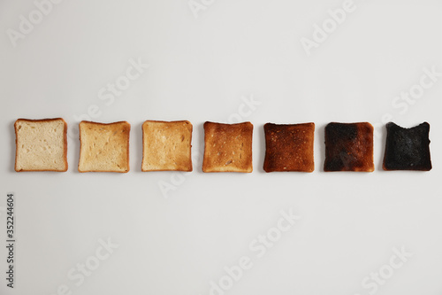 Tasty toasted slices of bread from unroasted to burnt. Stages of toastiness. Selective focus. Crusty delicious snack. White background. Set of toasts each toasted for longer time, degree of roasting.
