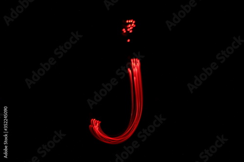 Long exposure photograph of the letter j in neon red colour fairy lights against a black background. Light painting photography. Part of an alphabet series. 