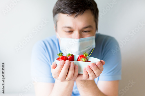 Close up Young Man in medical mask holding bowl with strawberry. man in an anti-virus medical mask . recovery from coronavirus. stop COVID-19 pandemic