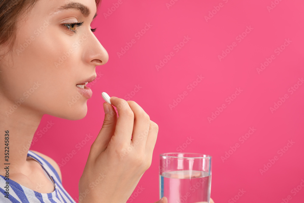 Young woman with glass of water taking vitamin pill on pink background. Space for text Young woman with glass of water taking vitamin pill on pink background. Space for text