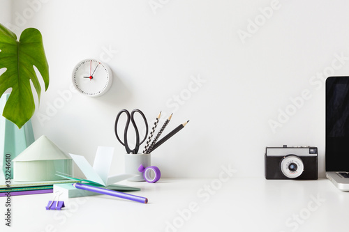 Creative desk with a blank picture frame or poster, desk objects, office supplies, books, and plant on a white background. 