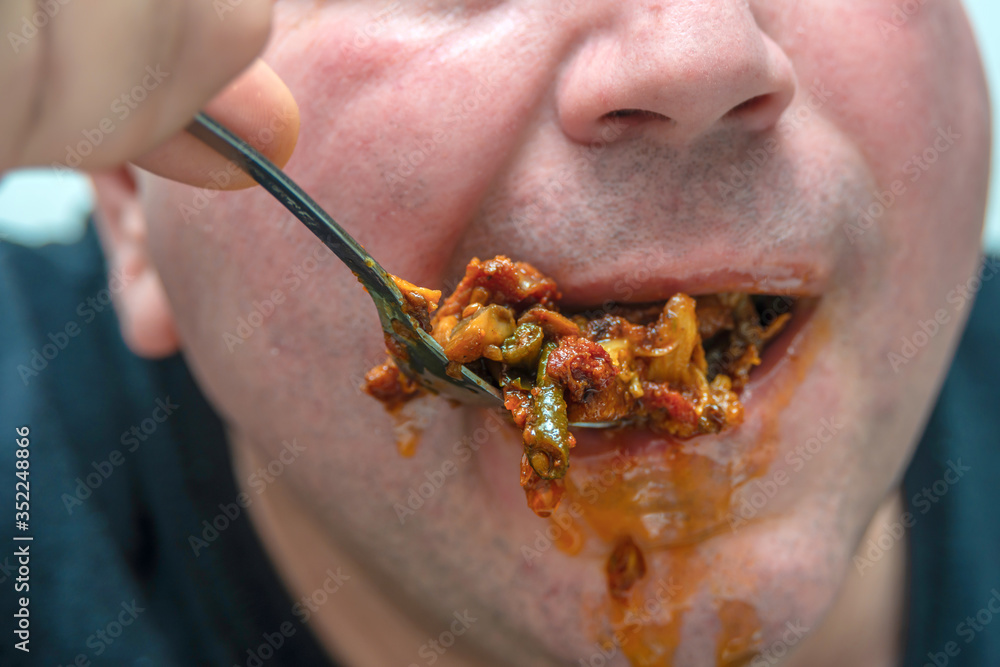 A hungry and fat fat man eagerly eats roasted meat with spices, fat from his mouth flows through his beard.