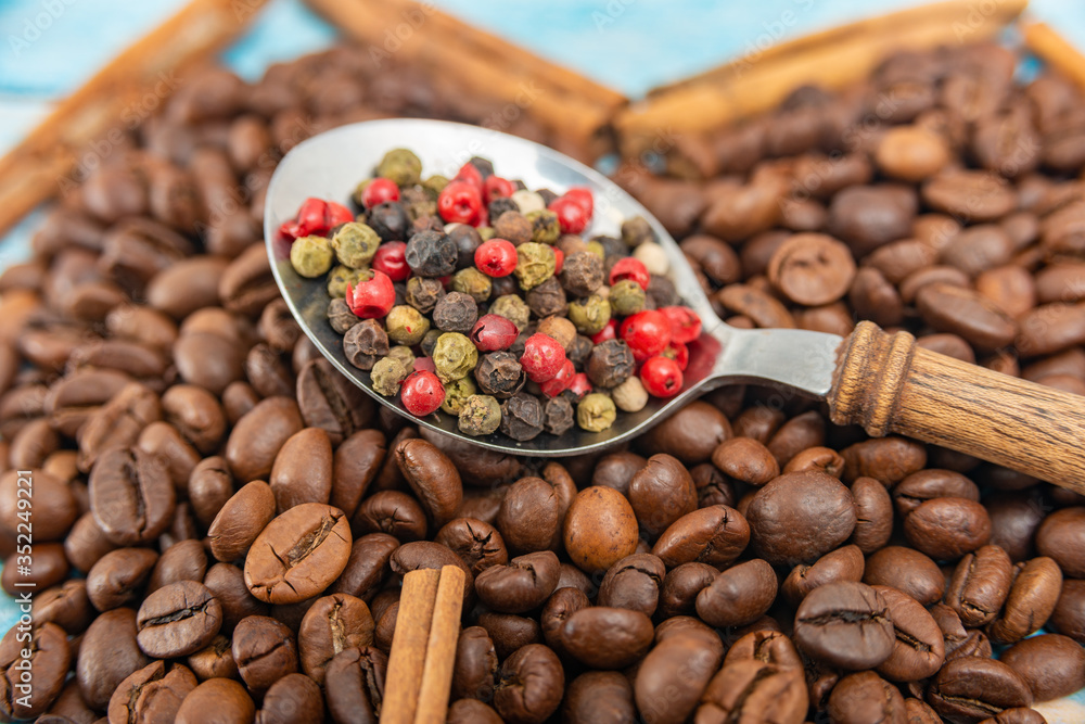 A spoon with a wooden handle with spices lies roasted coffee beans on a blue wooden background. A spoon with a wooden handle with spices lies roasted coffee beans on a blue wooden background.