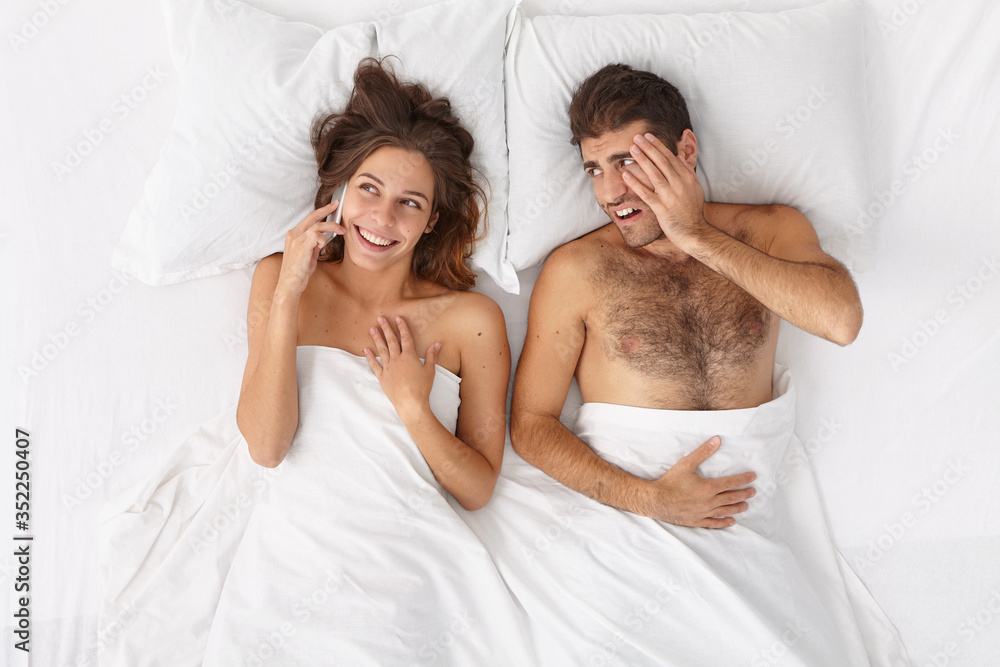 Φωτογραφία Talkative woman has telephone talk via modern cellphone, doesnt pay attention to husband who lies irritated and bored in bed, needs communication
