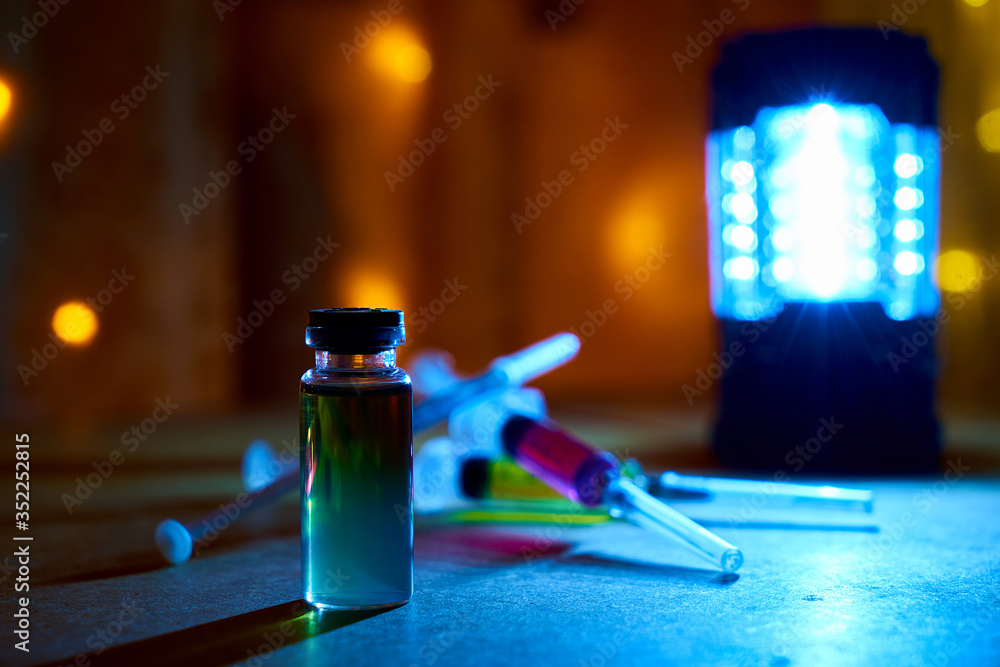 Bottle of Opium and Syringes with Drugs. In syringes and a bottle, the liquid is yellow, blue, purple. Drugs on old plywood in a dark room. Items are lit by cold and warm light. Health Danger of Drugs Bottle of Opium and Syringes with Drugs. In syringes and a bottle, the liquid is yellow, blue, purple. Drugs on old plywood in a dark room. Items are lit by cold and warm light. Health Danger of Drugs