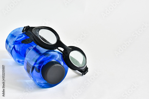 Swimming glasses and a bottle for water on a white background, place for text
