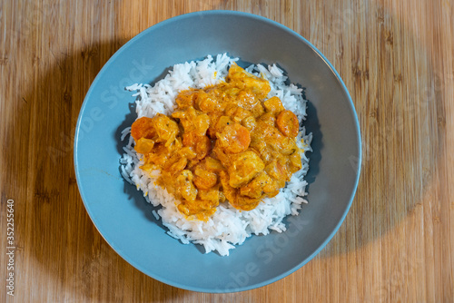 Plate of white rice with chicken and curry sauce on a wooden table.