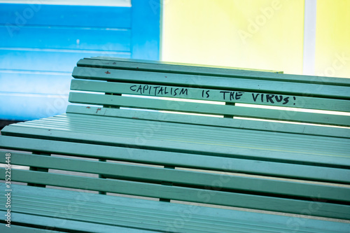 Wall Mural protest message against capitalism and the corona virus is written on a bench