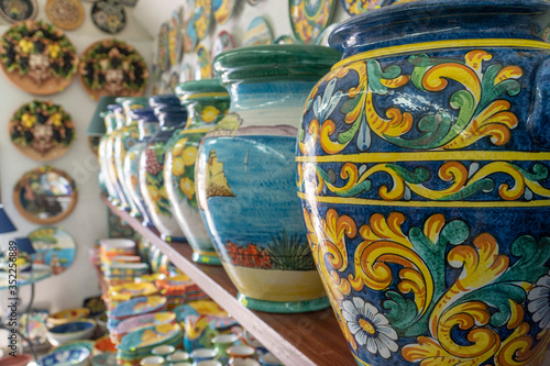 Close up on a handcrafted ceramic vase in amazing vivid colors and design. Many colorful souvenirs on shelf at a store in Vietri, Italy, selling other traditional pottery gifts