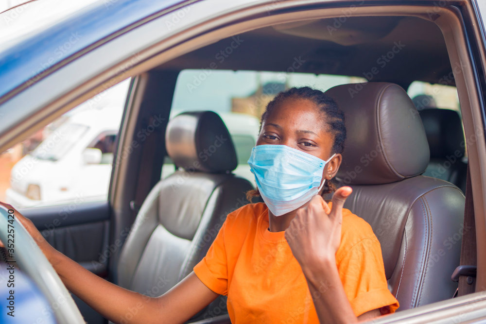 young beautiful african lady in a vehicle wearing face mask to prevent, preventing, prevented herself from the outbreak in the society and did thumbs up young beautiful african lady in a vehicle wearing face mask to prevent, preventing, prevented herself from the outbreak in the society and did thumbs up