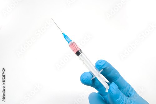 a doctor's hand in a blue glove holds a syringe up with a needle with a vaccine against the virus on a white background