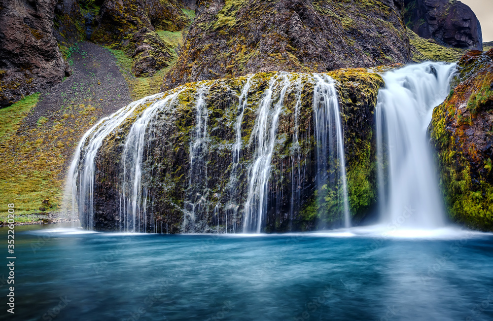 Obraz premium Wonderful nature of Iceland. fantastic view on canyon with green grass and icelandic moss near river with waterfall. Tipical Icelandic scenery. Stjornarfoss Waterfall during sunset. Wallpaper