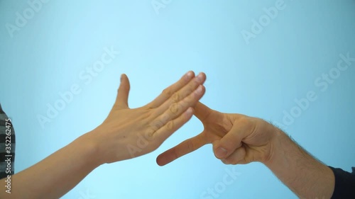Close up hands of young couple playing rock paper scissors on blue background indoors.