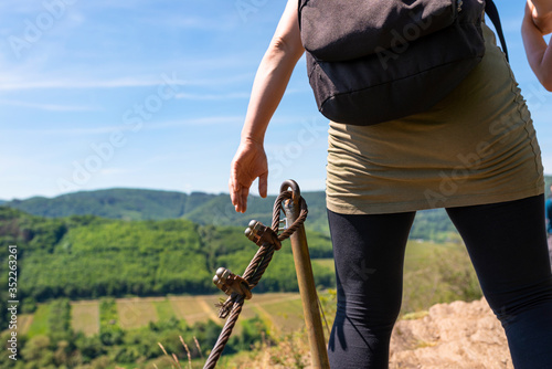 A woman walking a trail through the vineyards on a rocky, slate surface at a metal railing.