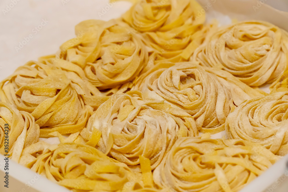 Macro and close up on freshly hand made plain floury pasta. Italian type of linguine, fettuccine or tagliatelle are formed in rolls ready to cook