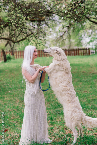 Blonde woman in white dress playing with her russian wolfhound dog in garden. photo