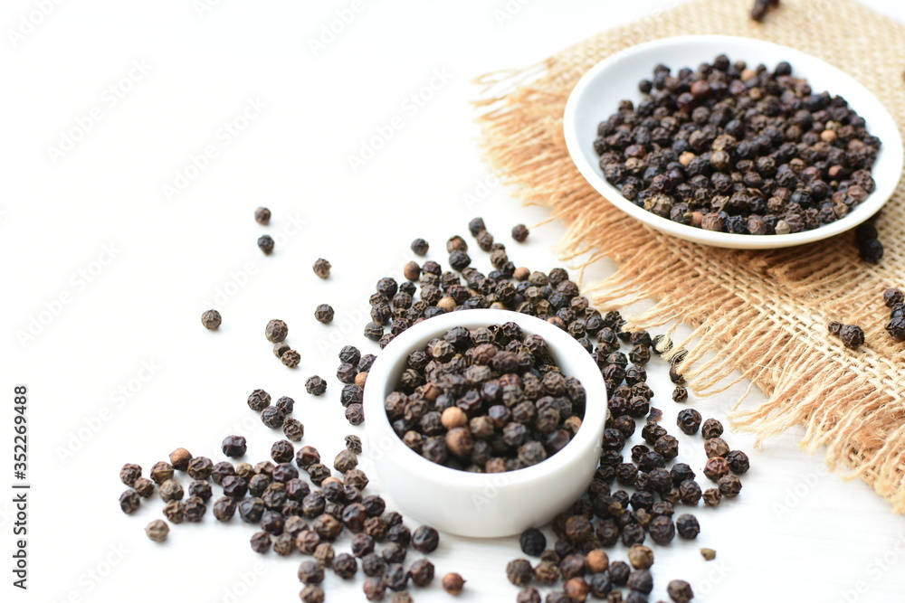 Black peppercorns in bowls on white wooden background Black peppercorns in bowls on white wooden background