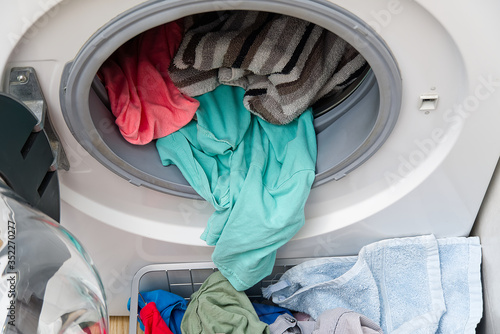 white front-loading washing machine, full of clothes. cleaning laundry. dirty laundry in the washing machine.
