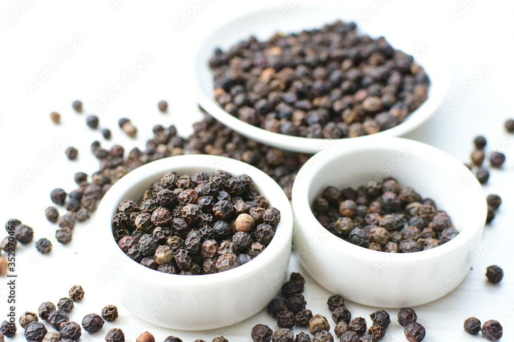 Black peppercorns in bowls on white wooden background Black peppercorns in bowls on white wooden background