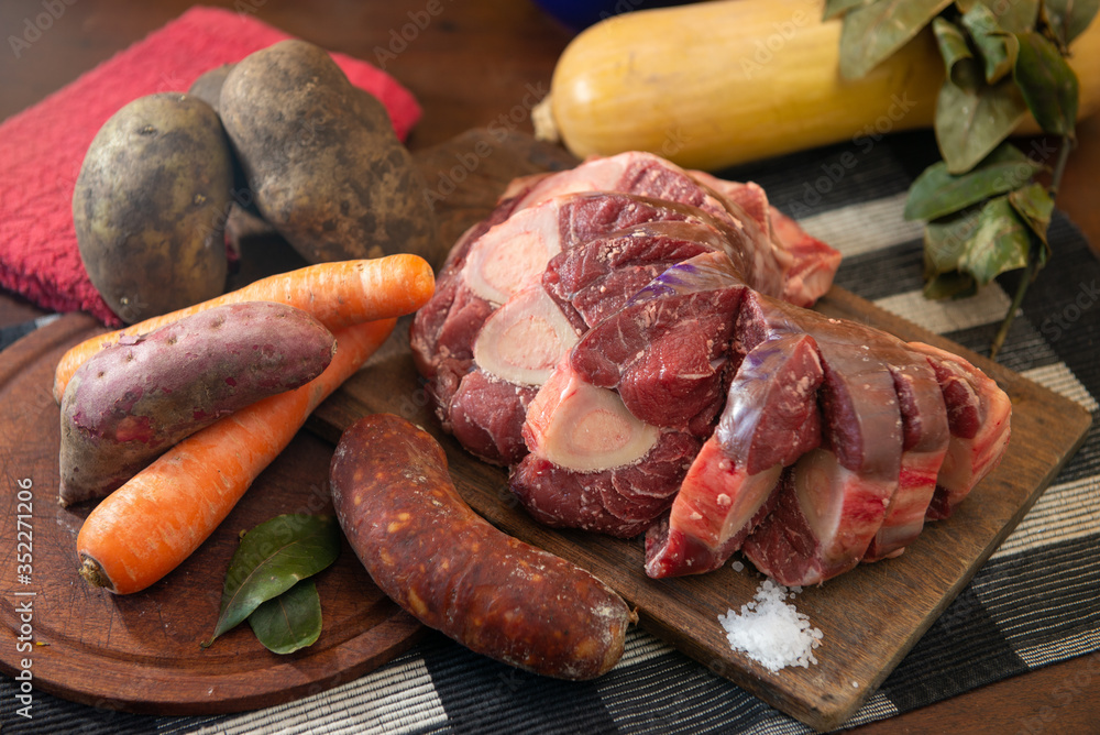Osobuco carne cruda y chorizo mas ingredientes para preparar un puchero o guiso sobre tabla de madera 