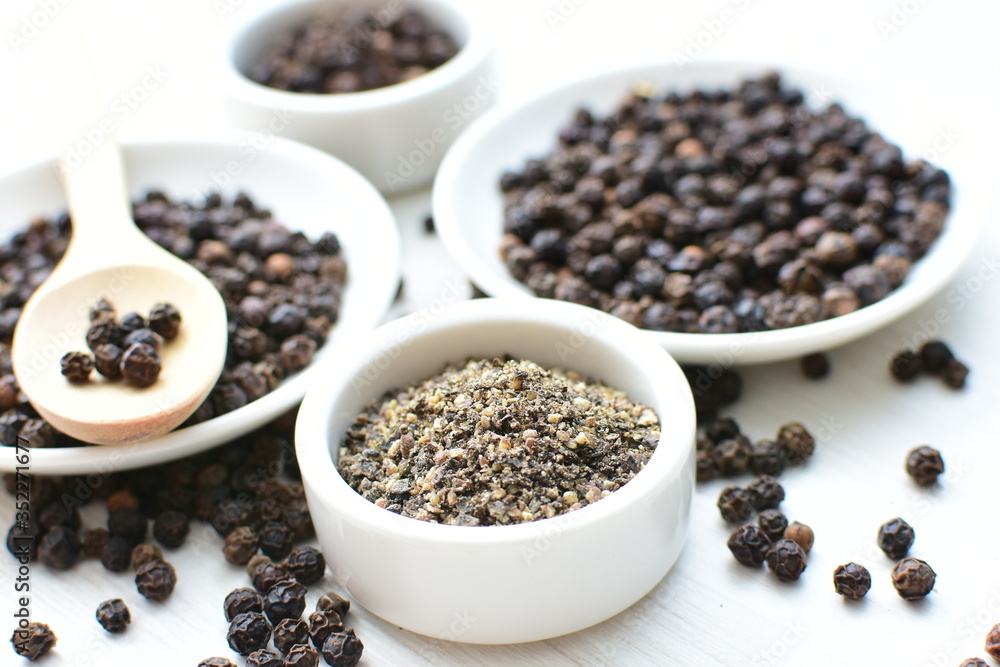 Black peppercorns in bowls on white wooden background Black peppercorns in bowls on white wooden background
