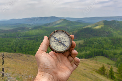 Male hand is holding a magnetic compass on the background of hills and the sky.