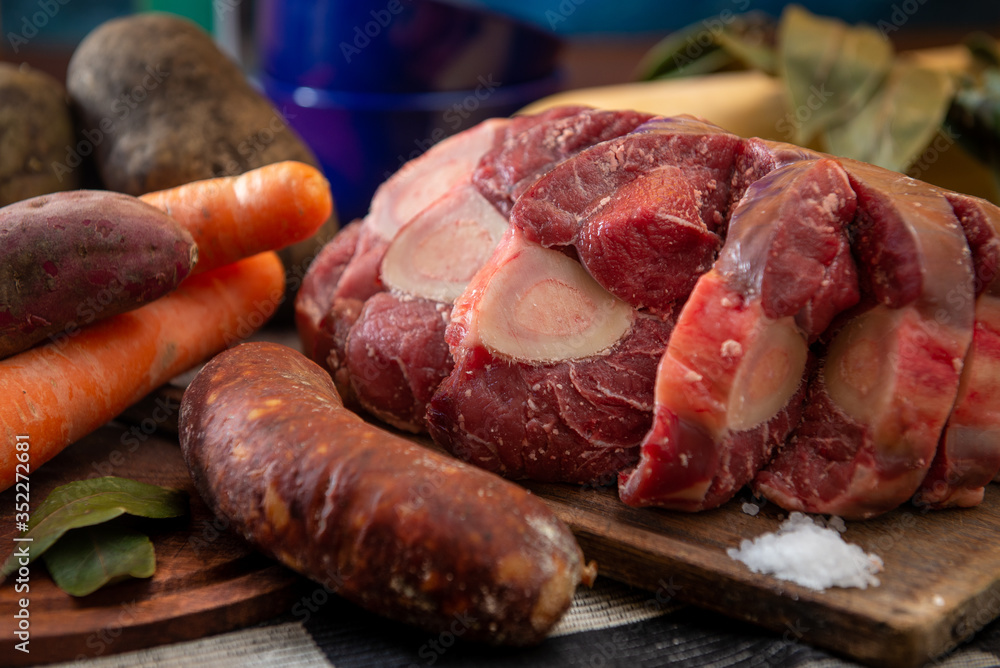 Osobuco carne cruda y chorizo mas ingredientes para preparar un puchero o guiso sobre tabla de madera Osobuco carne cruda y chorizo mas ingredientes para preparar un puchero o guiso sobre tabla de madera
