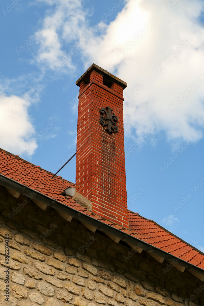 Old-year red brick chimney on a house roof.  Wrought iron decoration with a rounded shape.