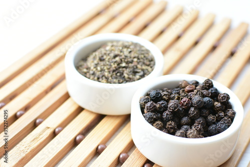 Black peppercorns in bowls on white wooden background