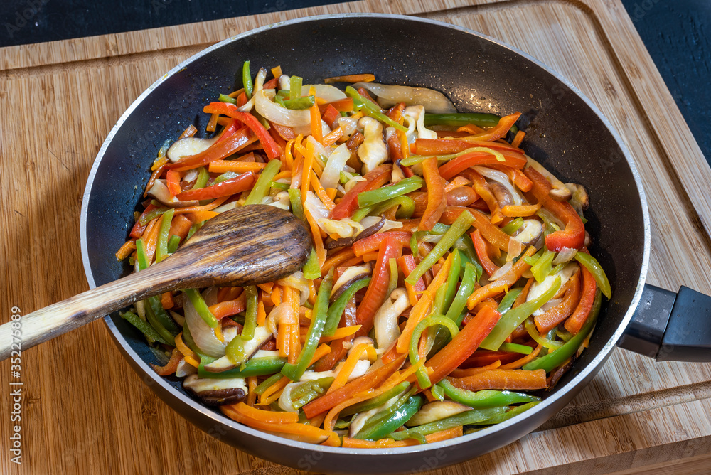 Black frying pan with different colored vegetables and shiitake mushrooms on a wooden table. Black frying pan with different colored vegetables and shiitake mushrooms on a wooden table.