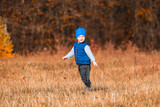 Toddler boy in a blue hat and blue vest on a background of bright orange forest in autumn.