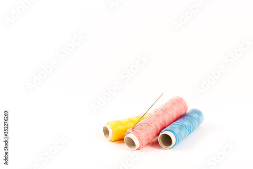 Three spools and bobbins of thread of yellow  blue and pink color with needles on a white background in a minimalistic style with a place for text. Items for needlework  embroidery and sewing.