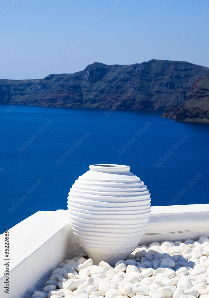 Santorini, Greece. White terrace with ceramic pot and pebbles against blue sea and sky background. - obrazy, fototapety, plakaty 