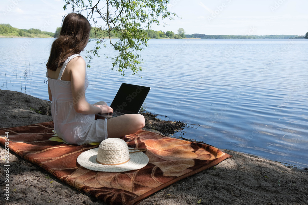 a young girl in a white dress sits on a lake, on her feet lies a laptop
