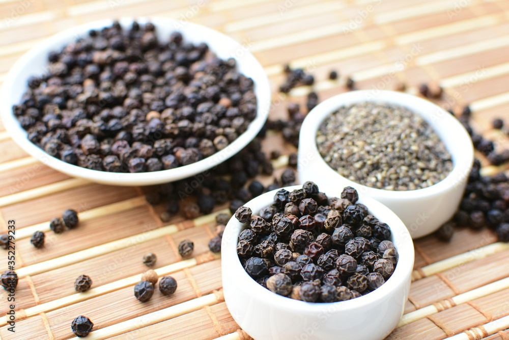 Whole and ground black peppercorns on white wooden background