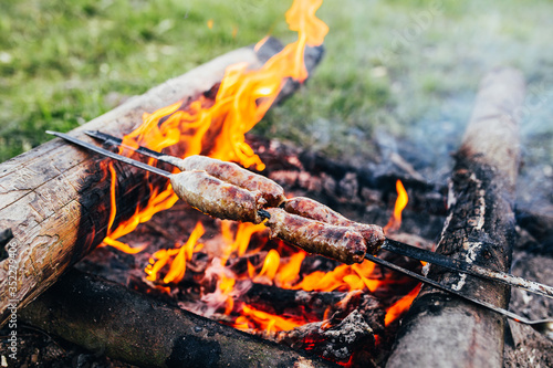 Rustic sausage on a skewer at the stake - sausages are fried over an open fire in the forest - camping food
