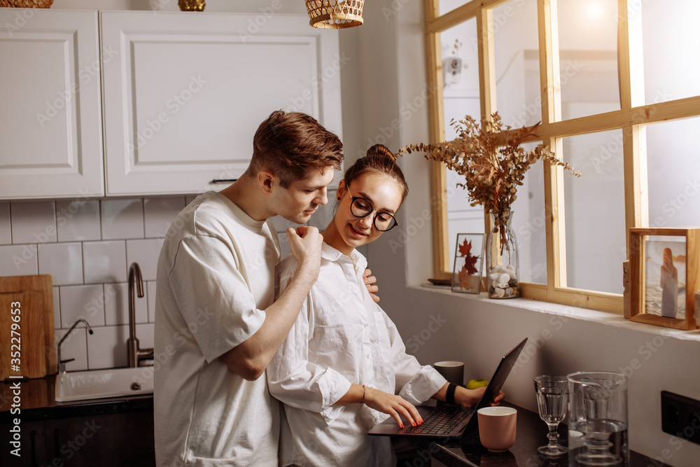 handsome caucasian caring guy support his working wife at home,woman stand using laptop, man hugs her from the back handsome caucasian caring guy support his working wife at home,woman stand using laptop, man hugs her from the back