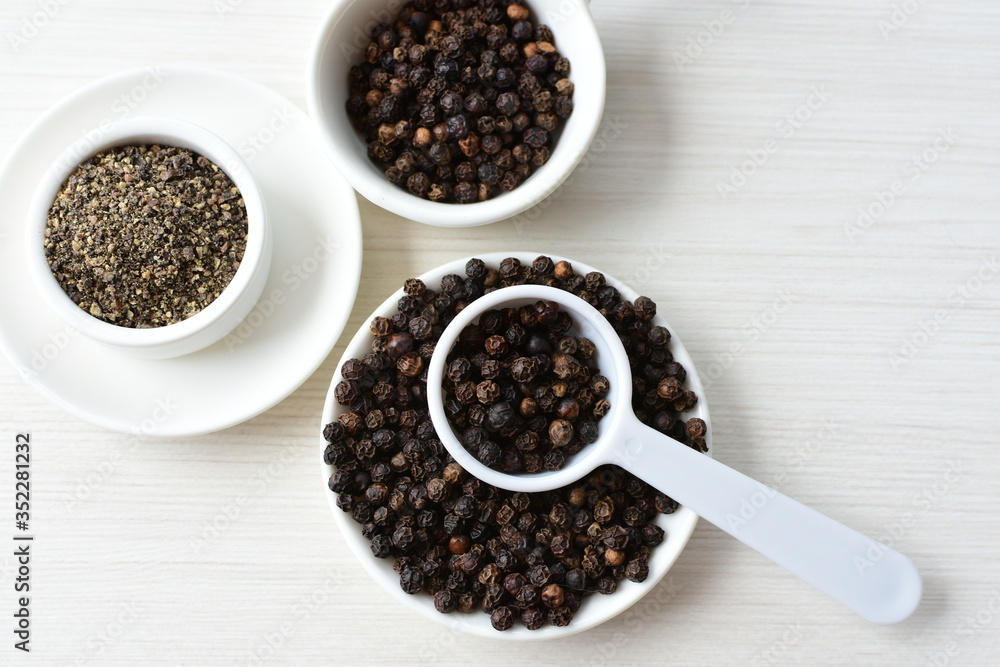 Whole and ground black peppercorns on white wooden background Whole and ground black peppercorns on white wooden background