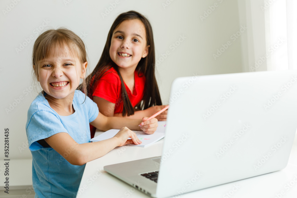 Cool online school. Kids studying online at home using a laptop. Cheerful young little girls using laptop computer studying through online e-learning system. Distance or remote learning Cool online school. Kids studying online at home using a laptop. Cheerful young little girls using laptop computer studying through online e-learning system. Distance or remote learning