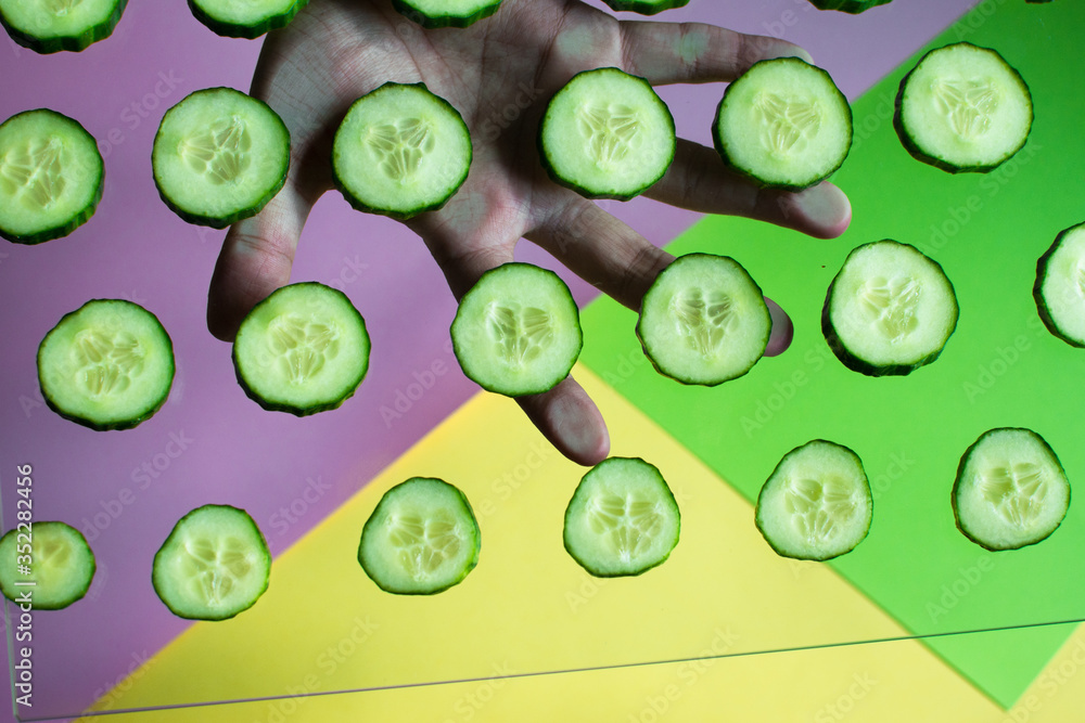hand holding a glass plate with a slice of cucumber on a multicolored background hand holding a glass plate with a slice of cucumber on a multicolored background