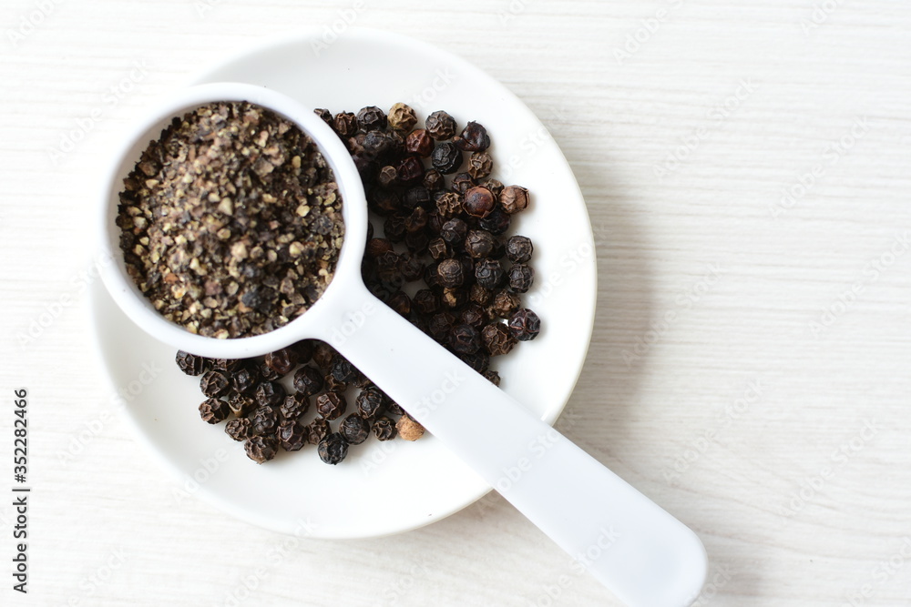 Whole and ground black peppercorns on white wooden background Whole and ground black peppercorns on white wooden background