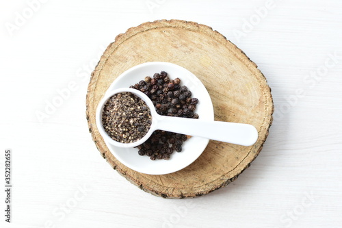 Whole and ground black peppercorns on white wooden background