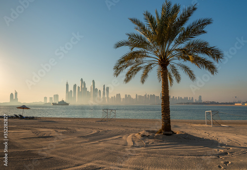 Sandy beach with palm tree and Dubai skyline view.