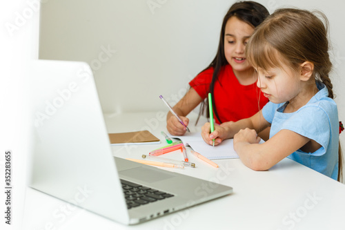 Two girls, the oldest and the youngest, are engaged at a table on a laptop.