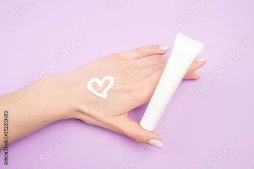 Hand cream isolated on lilac background. Cream heart on hand. Beauty concept.