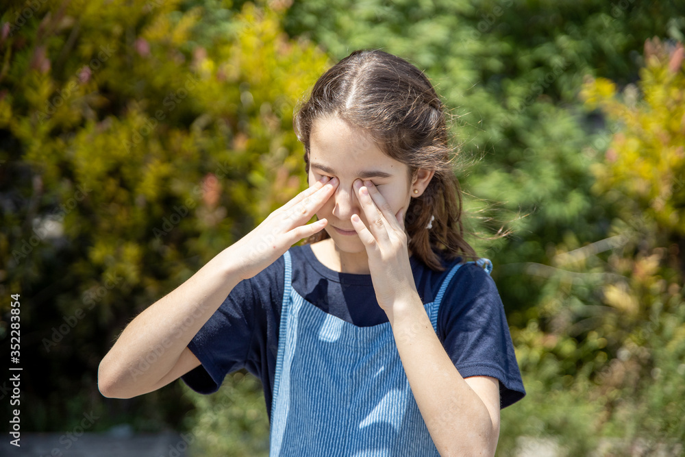 Little girl rubbing her eyes from an itchy allergy in the garden Little girl rubbing her eyes from an itchy allergy in the garden